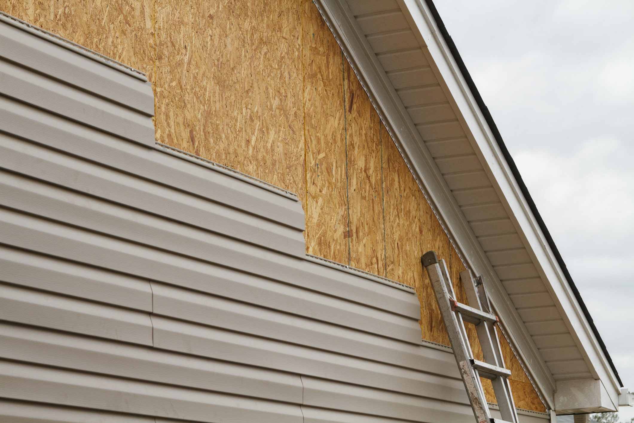 New beige vinyl siding being installed over an osb (oriented strand board) substrate on a residential house in the Southeastern USA region on a cloudy day. The old vinyl siding was being replaced after a hail storm.