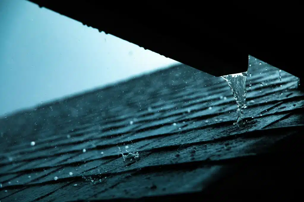 Rainwater pouring off roof shingles during heavy rainfall.